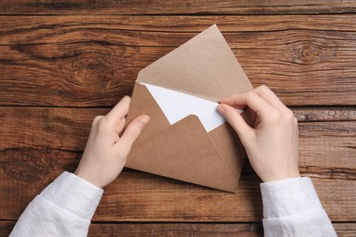 Woman taking card out of letter envelope at wooden table, top view