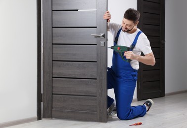 Photo of Worker in uniform with screw gun repairing door lock indoors