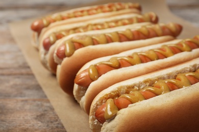 Photo of Hot dogs with mustard on wooden table, closeup