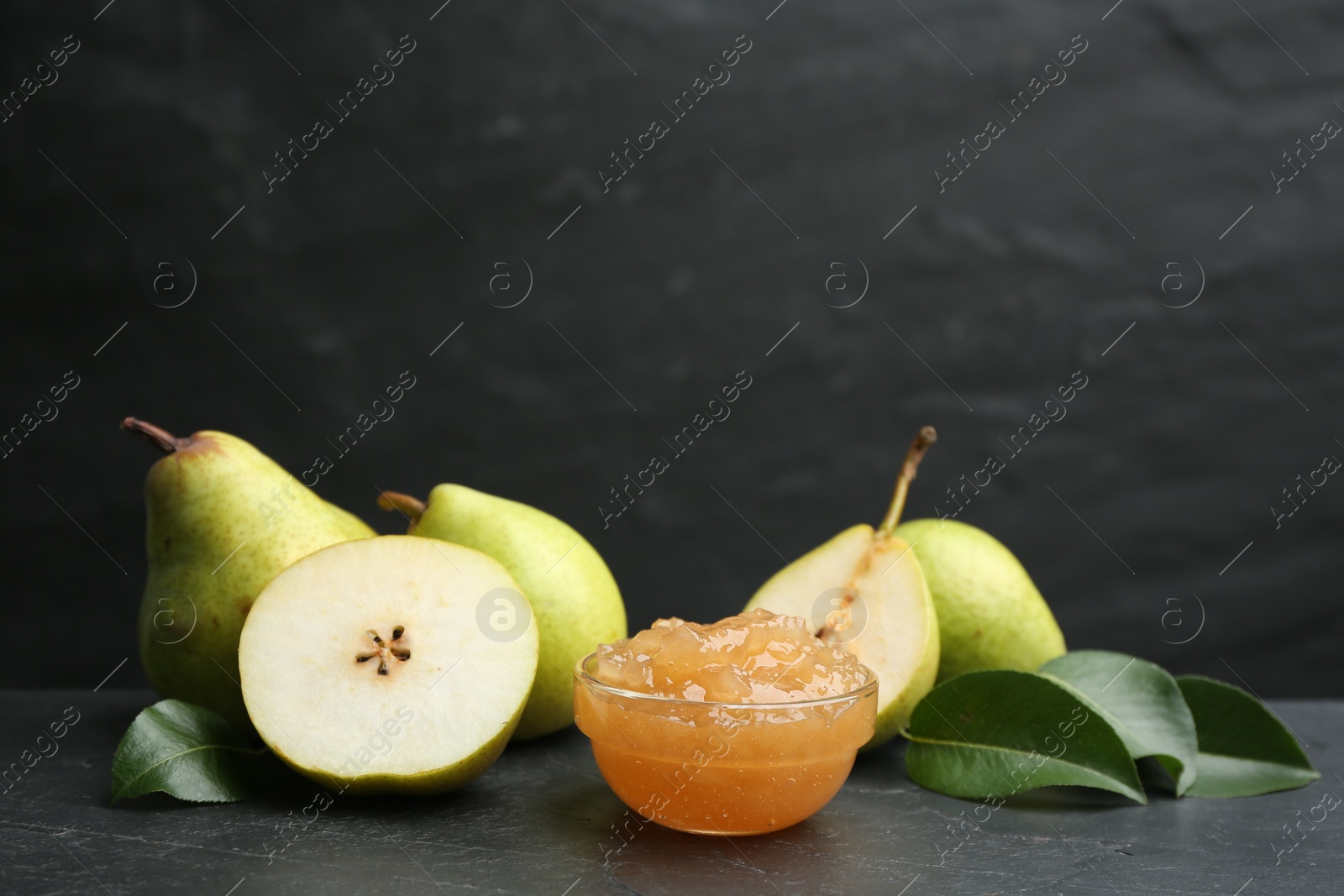 Photo of Tasty homemade pear jam and fresh fruits on black table. Space for text