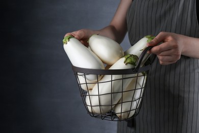 Photo of Woman holding metal basket with white eggplants on grey background, closeup. Space for text