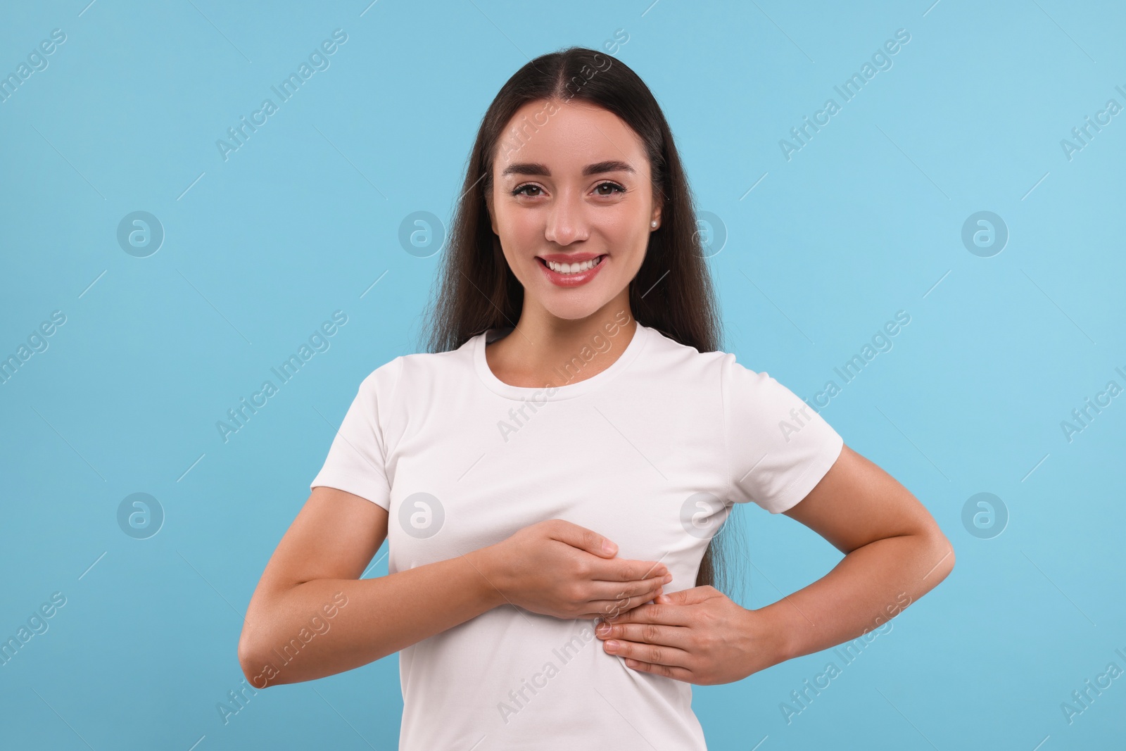 Photo of Beautiful happy woman doing breast self-examination on light blue background