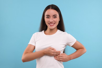 Beautiful happy woman doing breast self-examination on light blue background