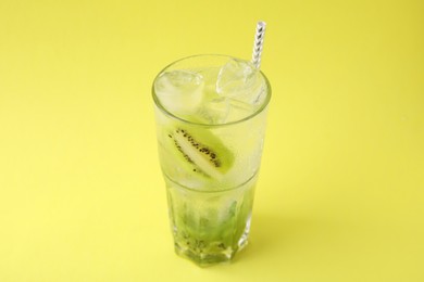 Glass of refreshing drink with kiwi on yellow background
