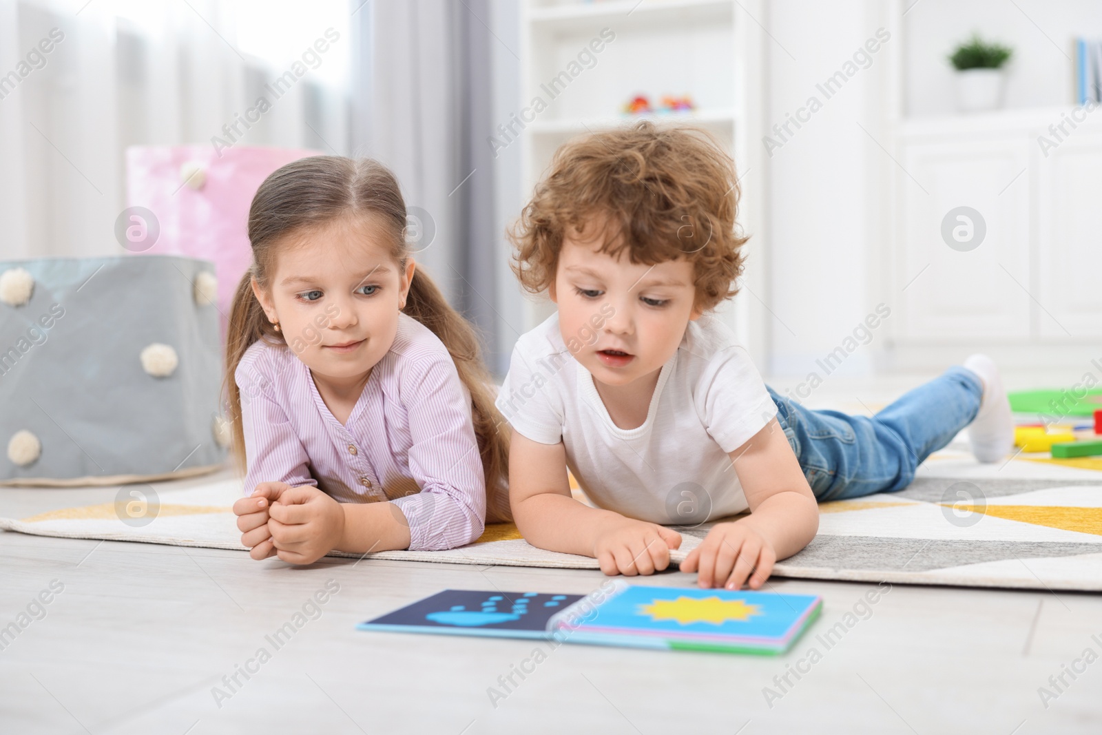 Photo of Cute little children reading book on floor in kindergarten