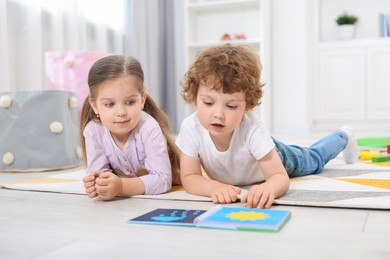 Cute little children reading book on floor in kindergarten