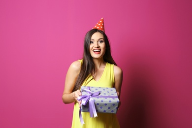 Young woman with birthday gift on color background