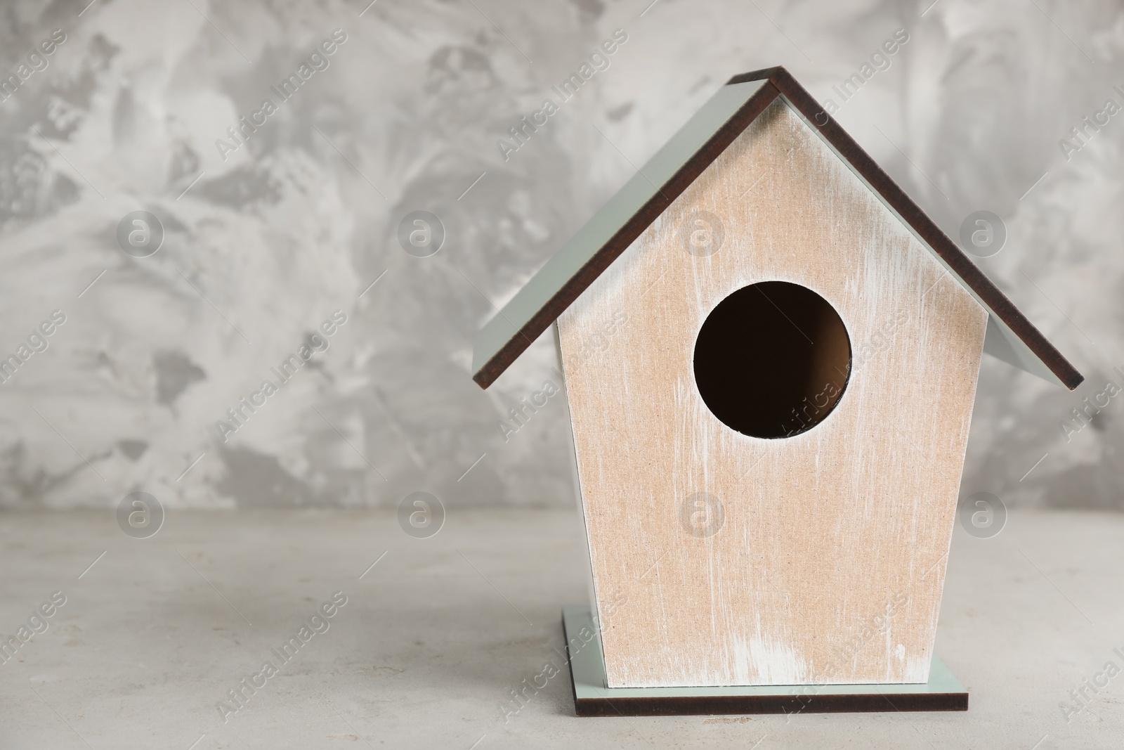 Photo of Beautiful bird house on light grey stone table, space for text