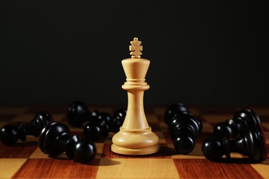 King among fallen black chess pieces on wooden board against dark background. Competition concept