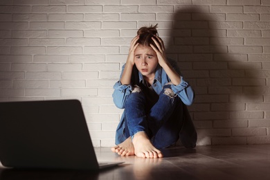 Photo of Shocked teenage girl with laptop on floor in dark room. Danger of internet