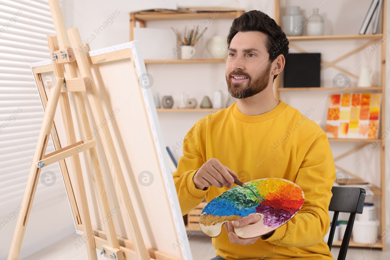 Photo of Man painting in studio. Using easel to hold canvas