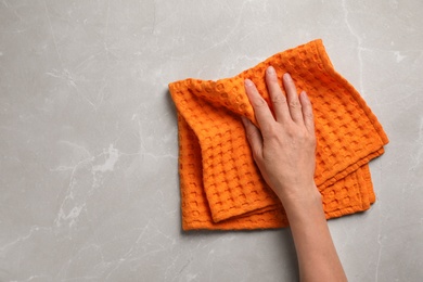 Photo of Woman wiping marble table with kitchen towel, top view. Space for text