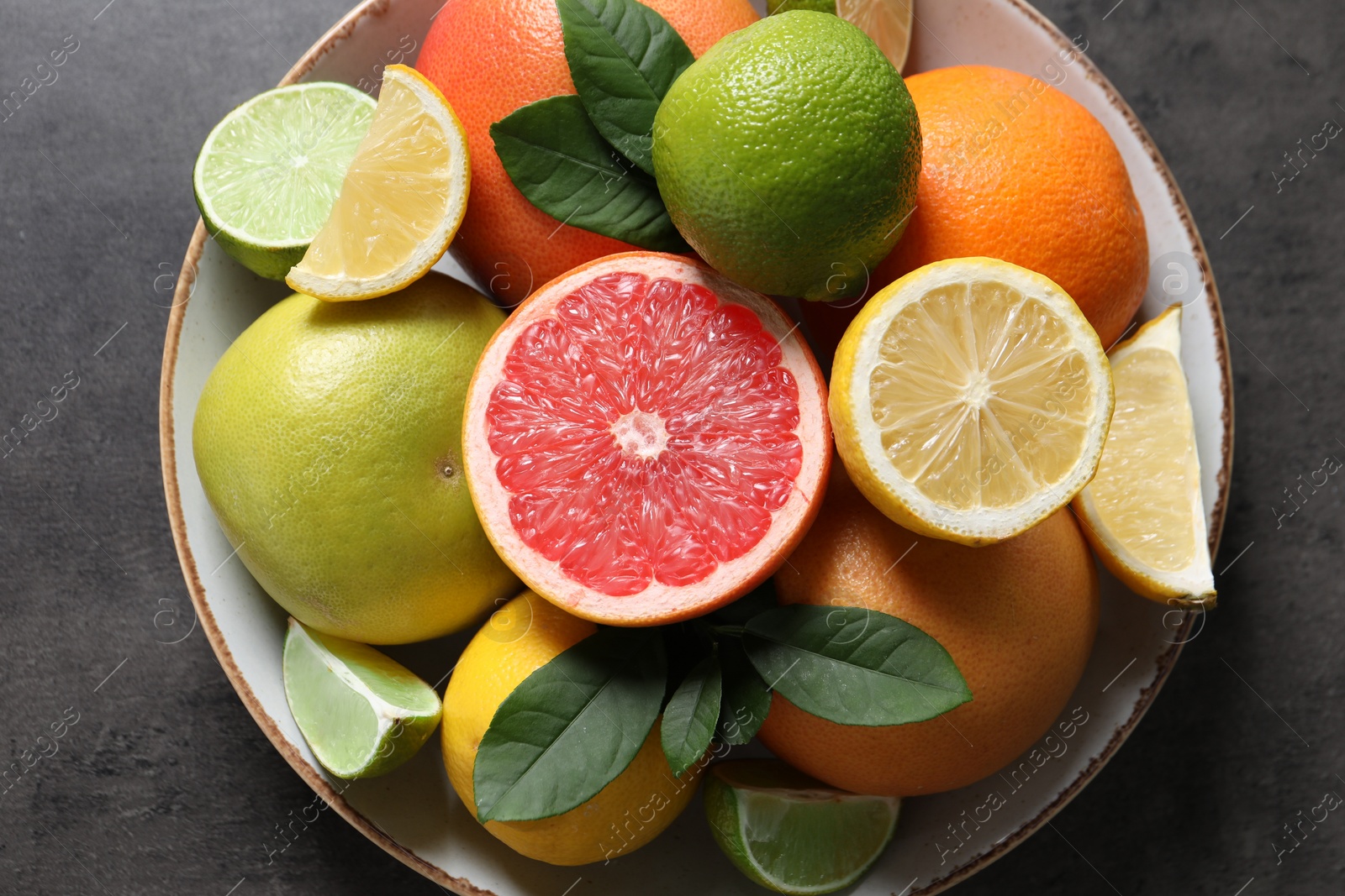 Photo of Different fresh citrus fruits and leaves on grey textured table, top view