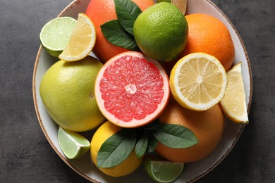 Photo of Different fresh citrus fruits and leaves on grey textured table, top view