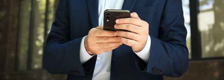 Image of Businessman typing message on mobile phone outdoors, closeup. Banner design