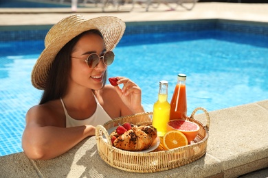 Photo of Young woman with delicious breakfast on tray in swimming pool