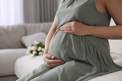 Photo of Young pregnant woman sitting on sofa at home, closeup