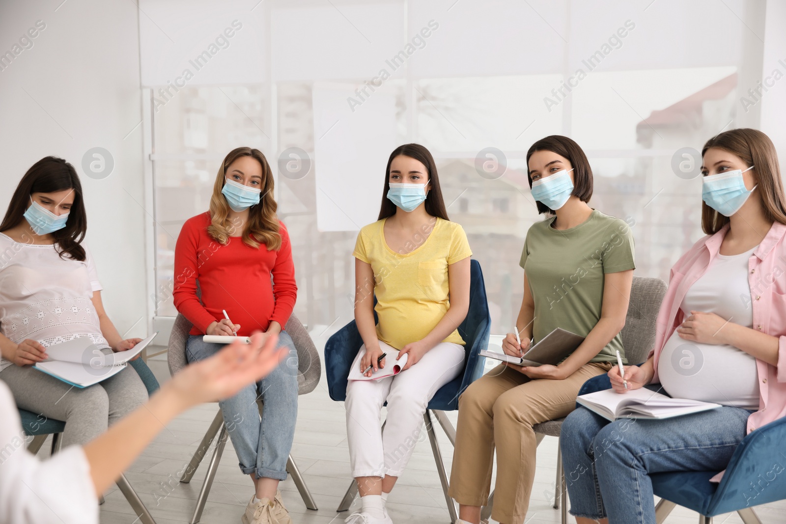 Photo of Group of pregnant women and midwife in protective masks at courses for expectant mothers indoors