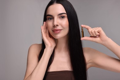 Beautiful young woman holding skincare ampoule on grey background