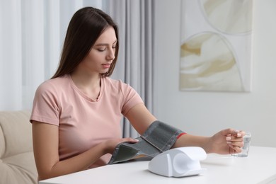 Photo of Woman measuring blood pressure with tonometer at home
