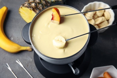 Photo of Dipping fruits into pot with white chocolate fondue on table