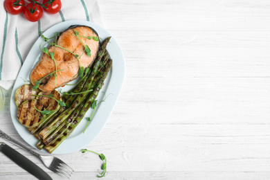 Photo of Tasty salmon steak served with grilled asparagus on white wooden table, flat lay. Space for text