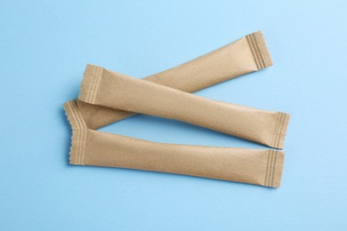 Photo of Beige sticks of sugar on light blue background, flat lay