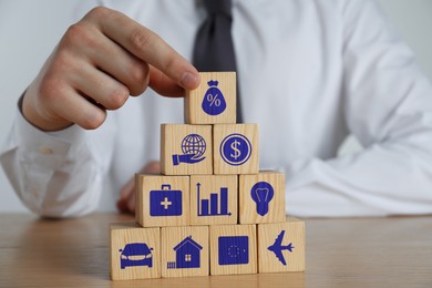 Man building pyramid of cubes with different icons at wooden table, closeup. Insurance concept