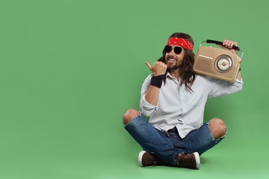 Photo of Stylish hippie man with retro radio receiver pointing at something on green background, space for text