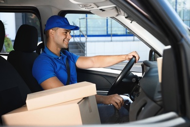 Photo of Young courier with parcels in delivery car