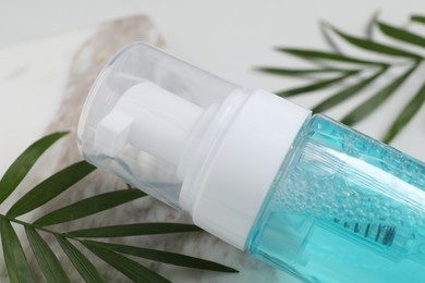 Bottle of face cleansing product and green leaves on table, closeup