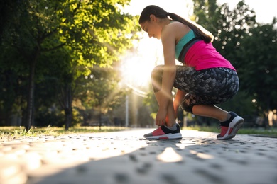 Photo of Young woman tying shoelaces before morning run in park. Space for text