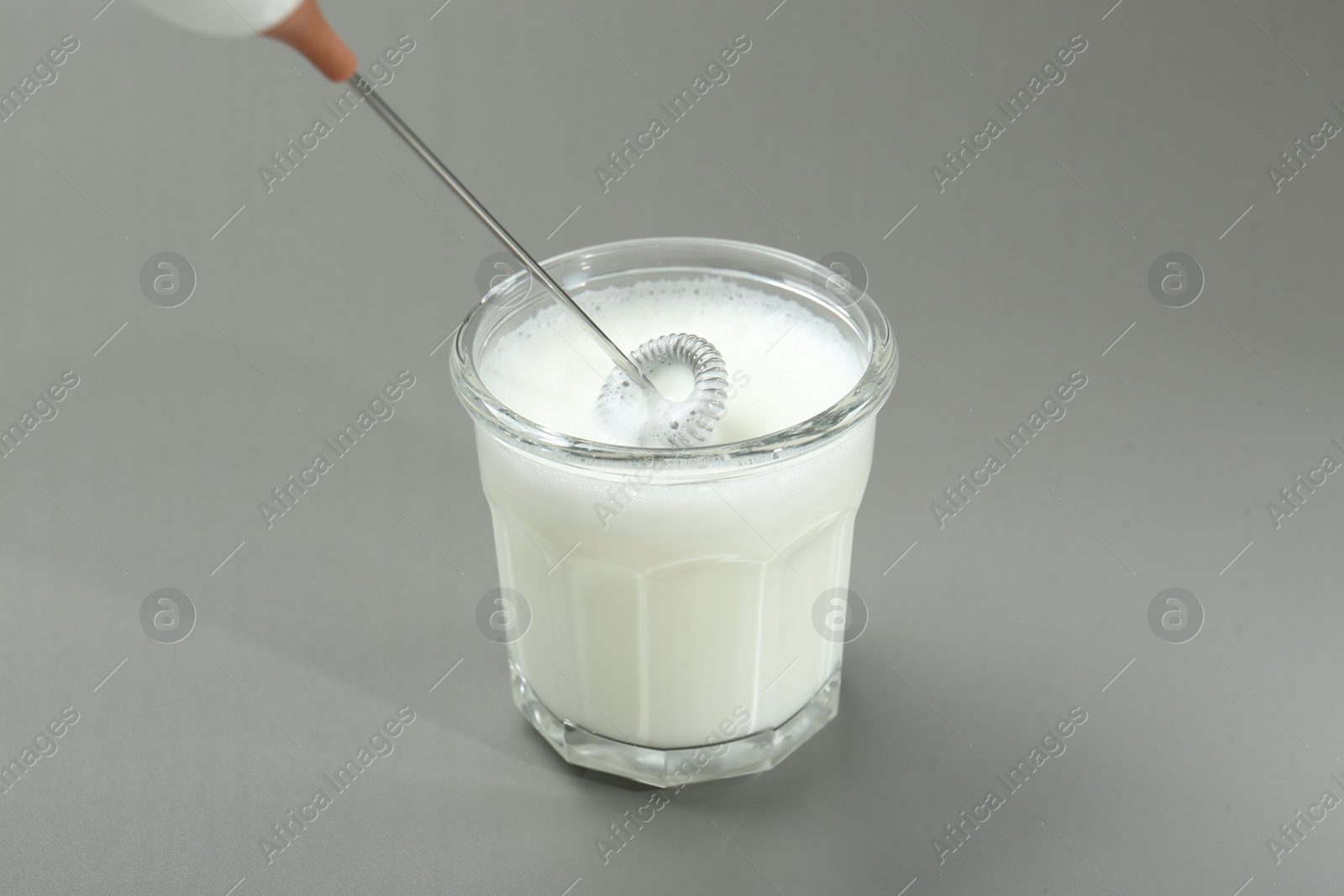 Photo of Whisking milk in glass with mini mixer (milk frother) on grey background, closeup