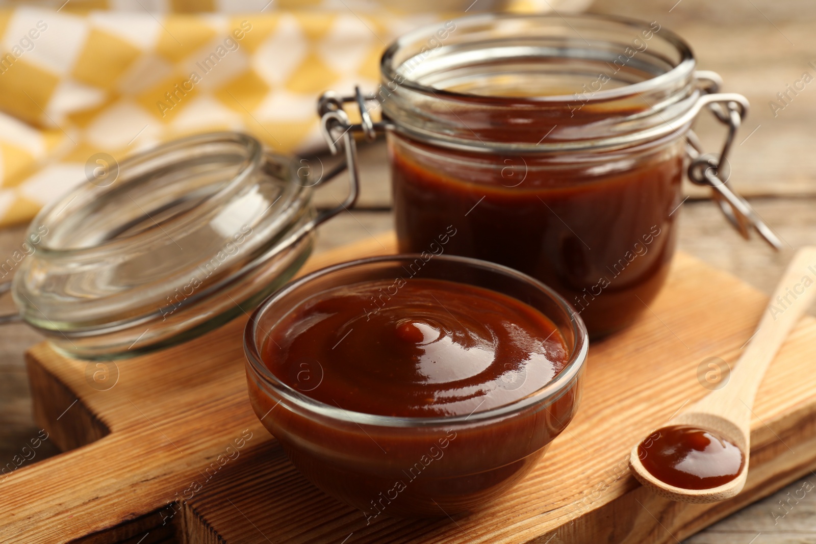Photo of Tasty barbeque sauce in bowl, jar and spoon on wooden table, closeup