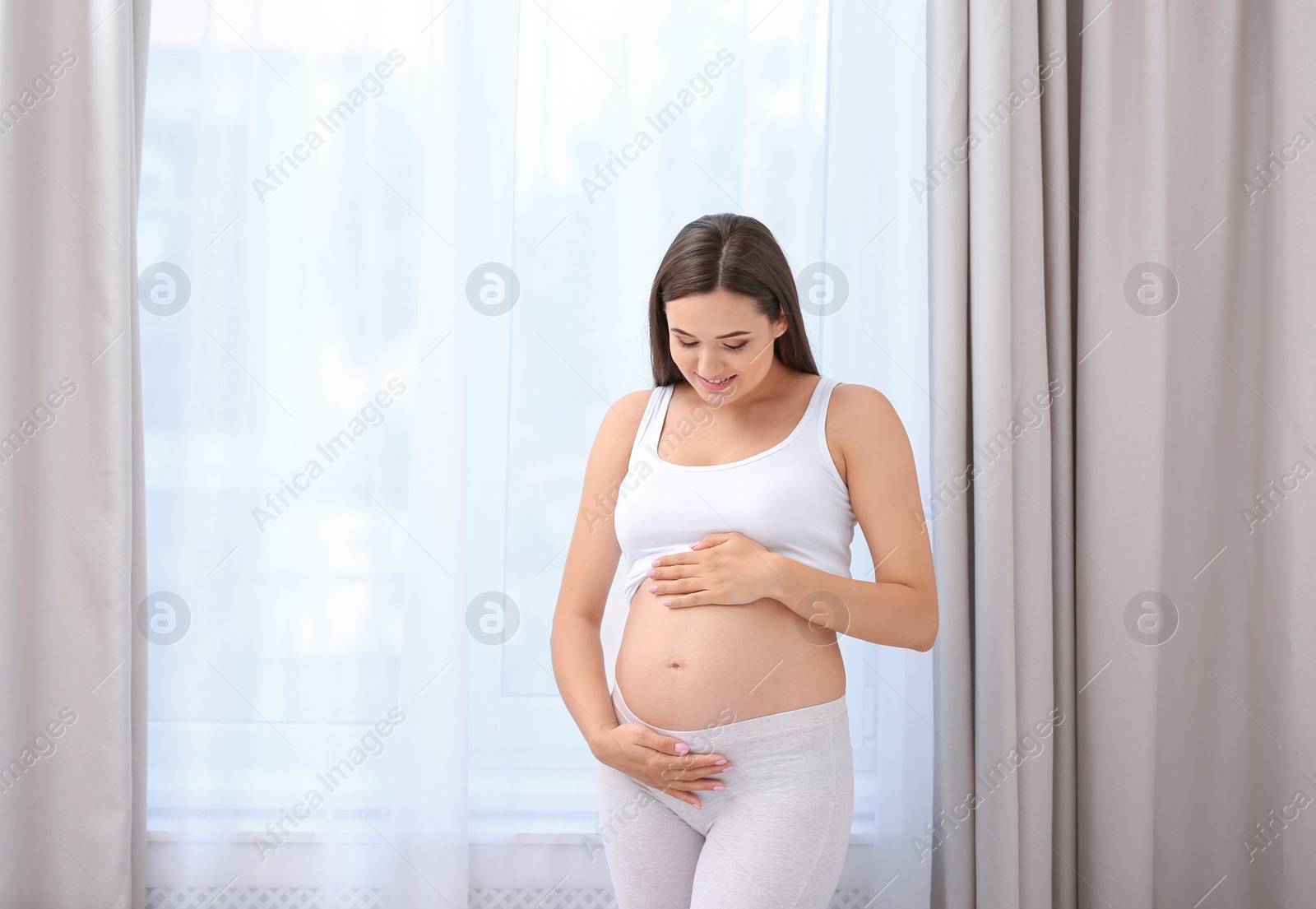 Photo of Young beautiful pregnant woman near window at home