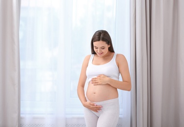 Young beautiful pregnant woman near window at home