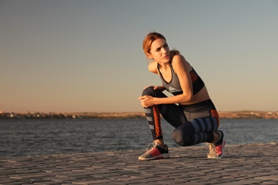 Photo of Young woman in sportswear having knee problems near river at sunset