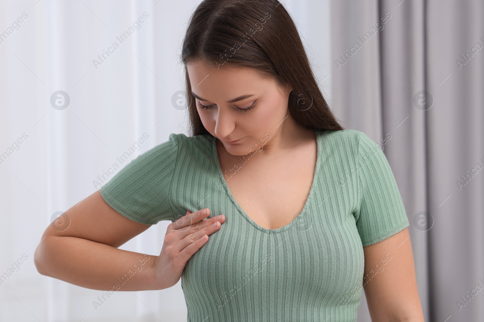 Photo of Mammology. Young woman doing breast self-examination indoors