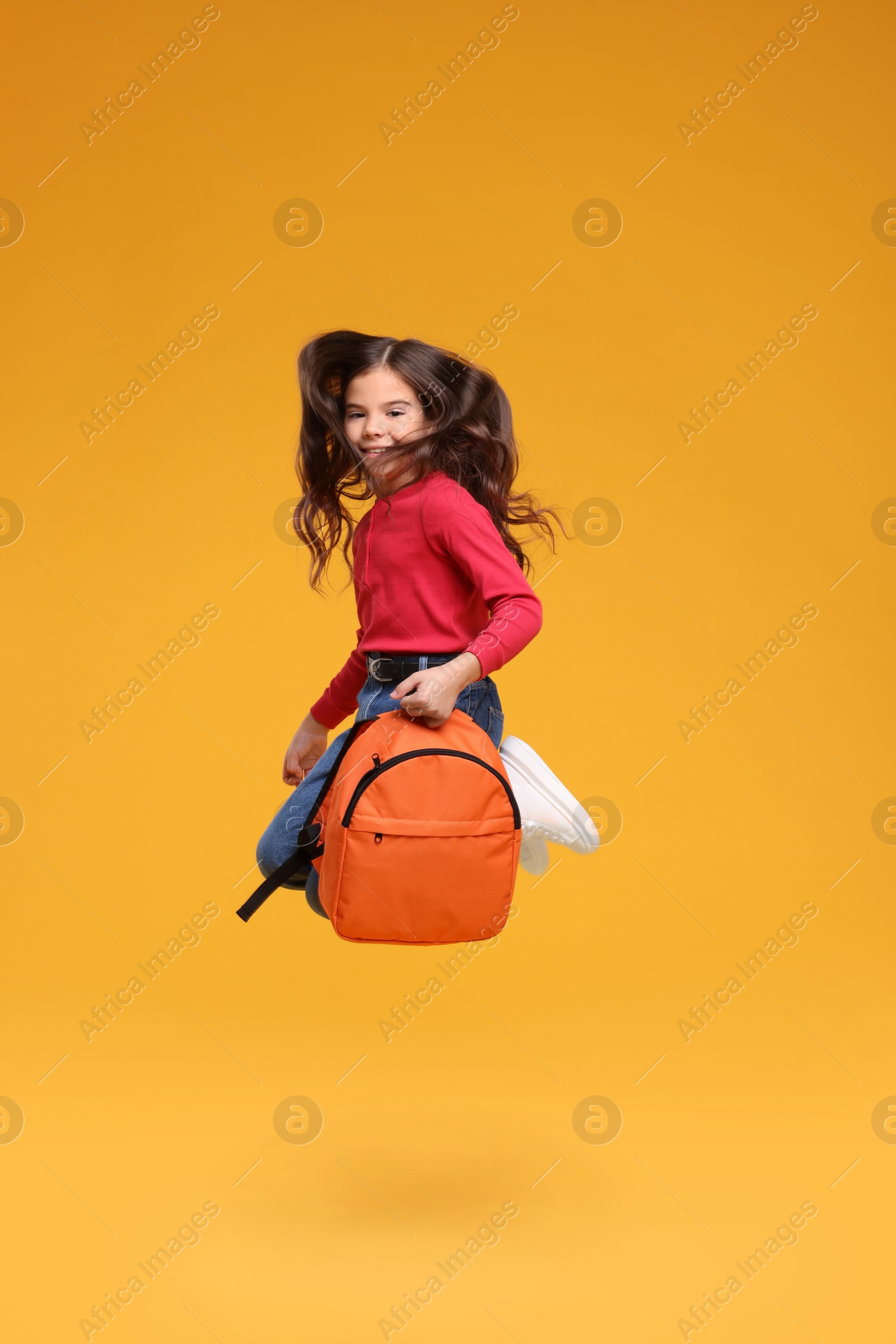 Photo of Back to school. Cute girl with backpack jumping on orange background