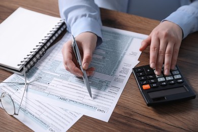 Payroll. Woman using calculator while working with tax return forms at wooden table, closeup