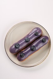 Photo of Delicious eclairs decorated with blueberries on white background, top view