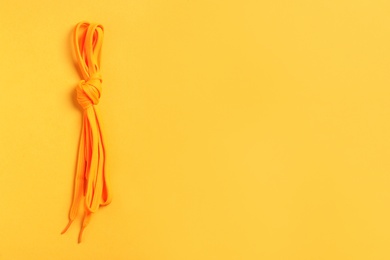 Photo of Orange shoelaces on yellow background, top view. Space for text