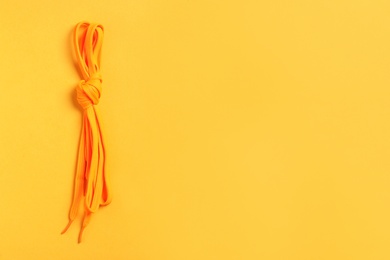 Orange shoelaces on yellow background, top view. Space for text