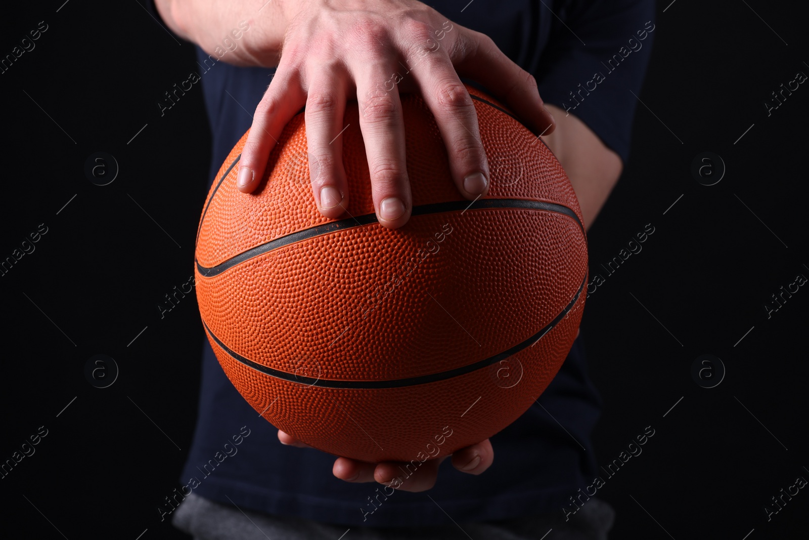 Photo of Athletic man with basketball ball on black background, closeup