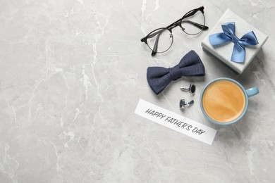 Photo of Card with phrase Happy Father's Day, cup of aromatic coffee, gift box and men accessories on light grey table, flat lay. Space for text