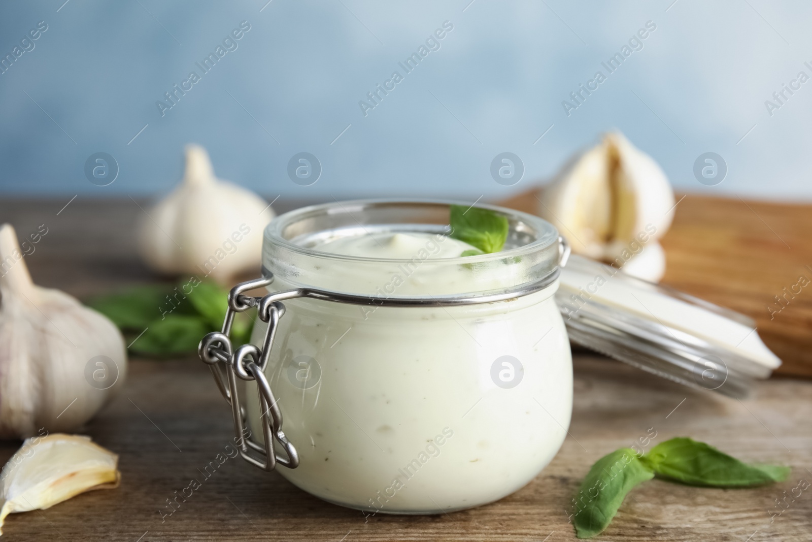 Photo of Composition with jar of garlic sauce on wooden table