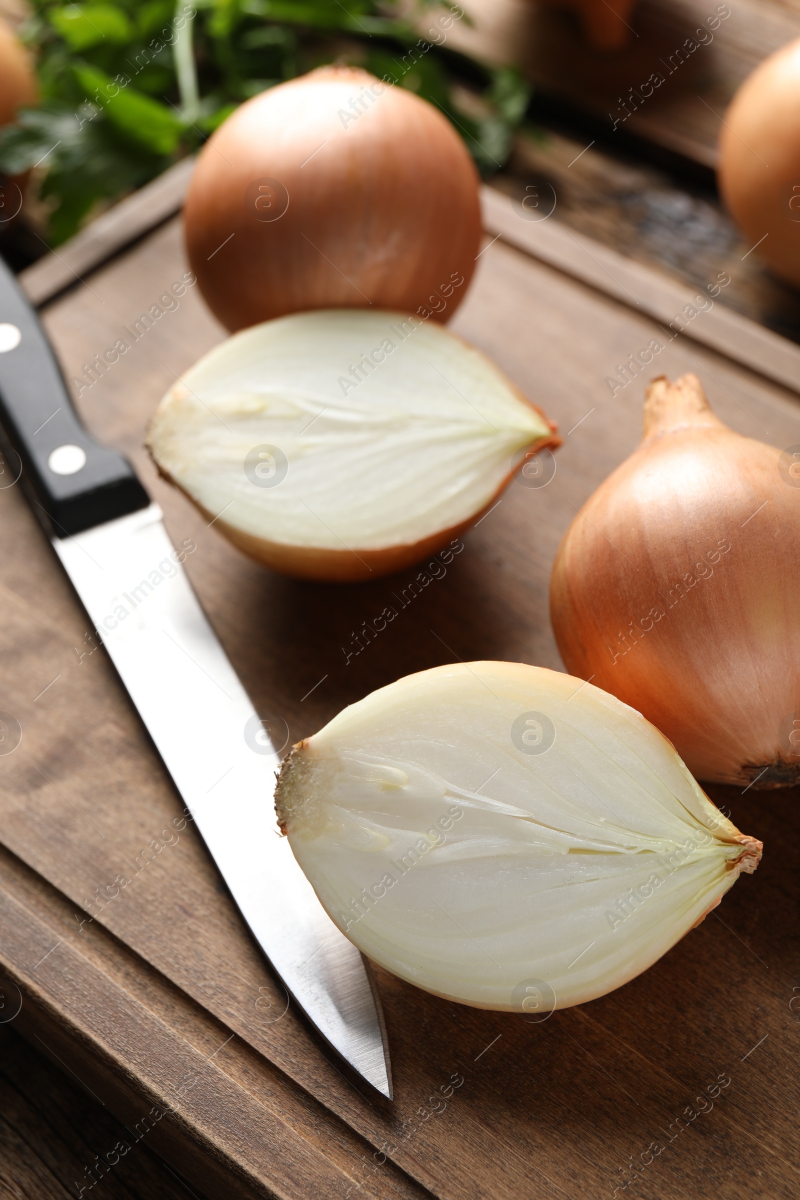 Photo of Whole and cut onions with knife on wooden board, closeup