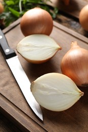 Whole and cut onions with knife on wooden board, closeup