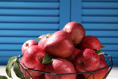 Photo of Metal bowl with wet red apples and green leaves on table, closeup