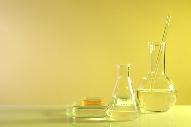 Photo of Laboratory analysis. Different glassware on table against yellow background, space for text